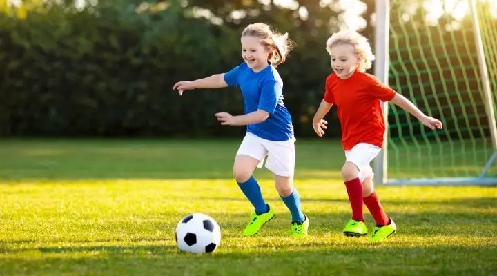 Two little girls, one in blue and one in red, happily chasing after a soccer ball
