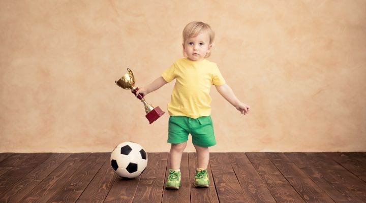 soccer award ideas 3 A toddler holding a trophy while a soccer ball is on the floor beside her
