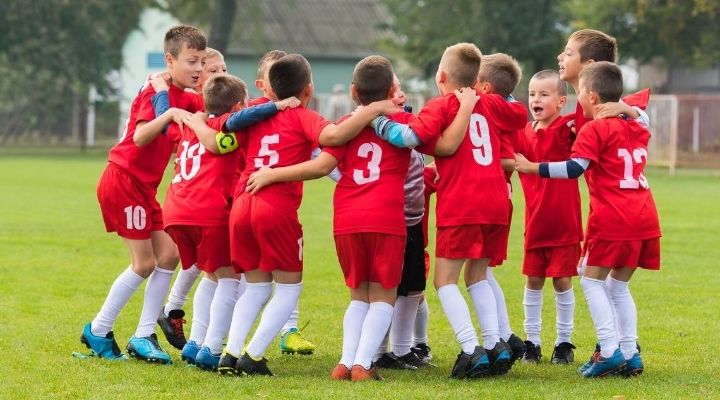 Soccer kids wearing red uniforms all gather in a huddle