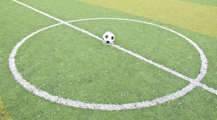 A soccer ball laying on the center of the football field