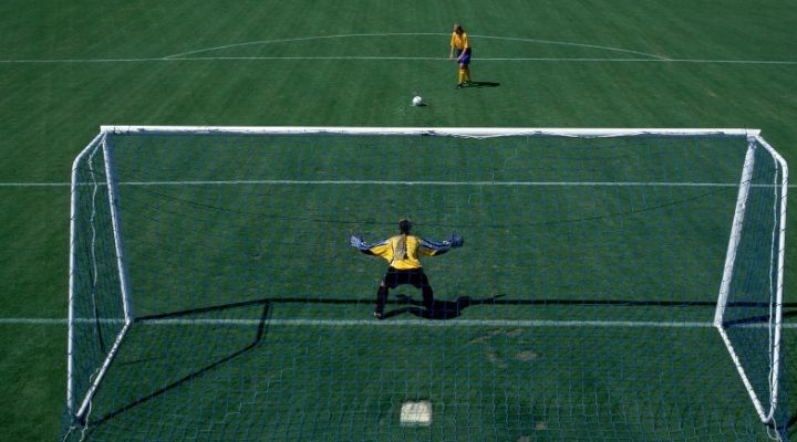 A female soccer player gets ready for a penalty kick while the goalkeeper has his arms spread wide in preparation for it