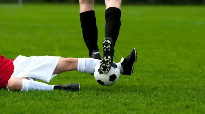A soccer player sliding on the ground in order to steal the ball from the opponent