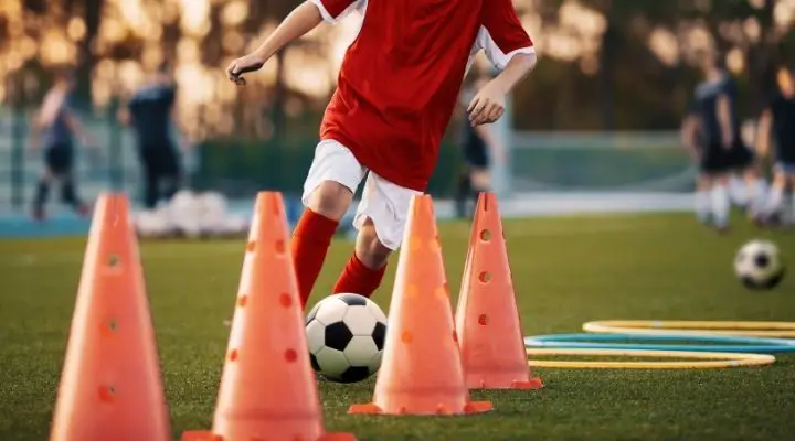 Soccer player in red jersey running between cones with a soccer ball at his feet
