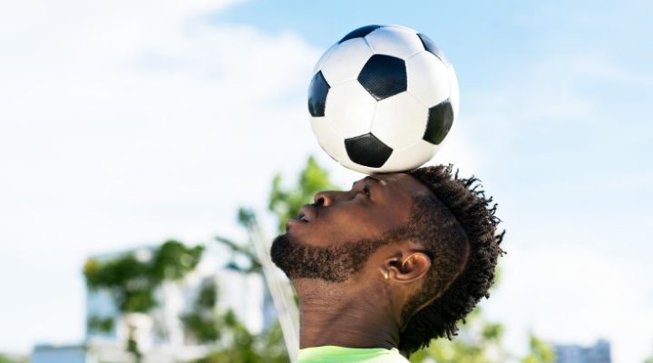 An African American soccer player balancing the ball on his head